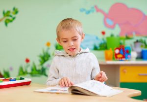 cute boy, kid with special needs looking at a book, in rehabilitation center