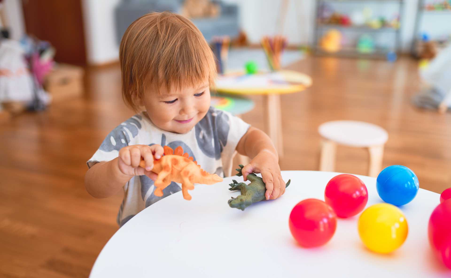 Adorable toddler playing with dinosaurs around lots of toys at kindergarten